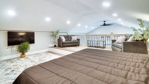 Ruime slaapkamer op zolder met een groot bed, twee sofa’s, een televisie en een balkon met een hekwerk.