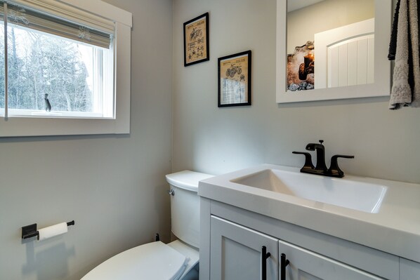 A bathroom with a toilet, sink, and window. - Modern Stark Home w/ Game Room, Grill & Fire Pit (Stark)