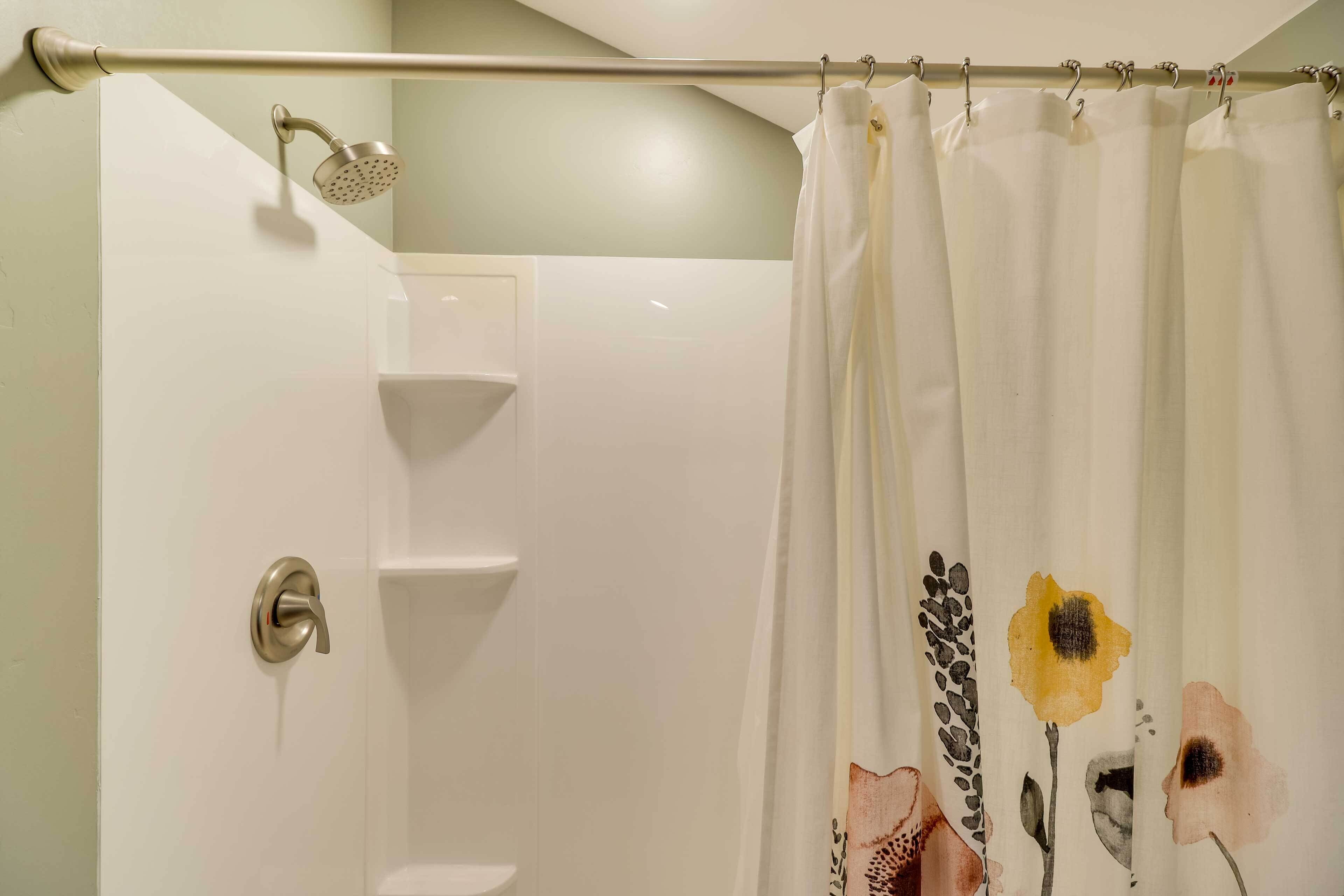A bathroom with a shower curtain featuring floral designs, a showerhead, and a towel rack.
