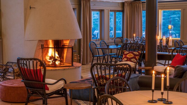 A cozy restaurant with a fireplace, comfortable seating, and large windows. - Norrfällsvikens Rum & Kök (Mjällom)