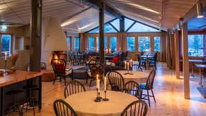 A spacious dining area with round tables, chairs, and a large window providing a view of the outdoors. - Norrfällsvikens Rum & Kök (Mjällom)