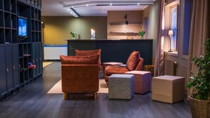 A modern lounge area with a dark wood floor, a sofa, a chair, and a small table with a candle. - Norrfällsvikens Rum & Kök (Mjällom)