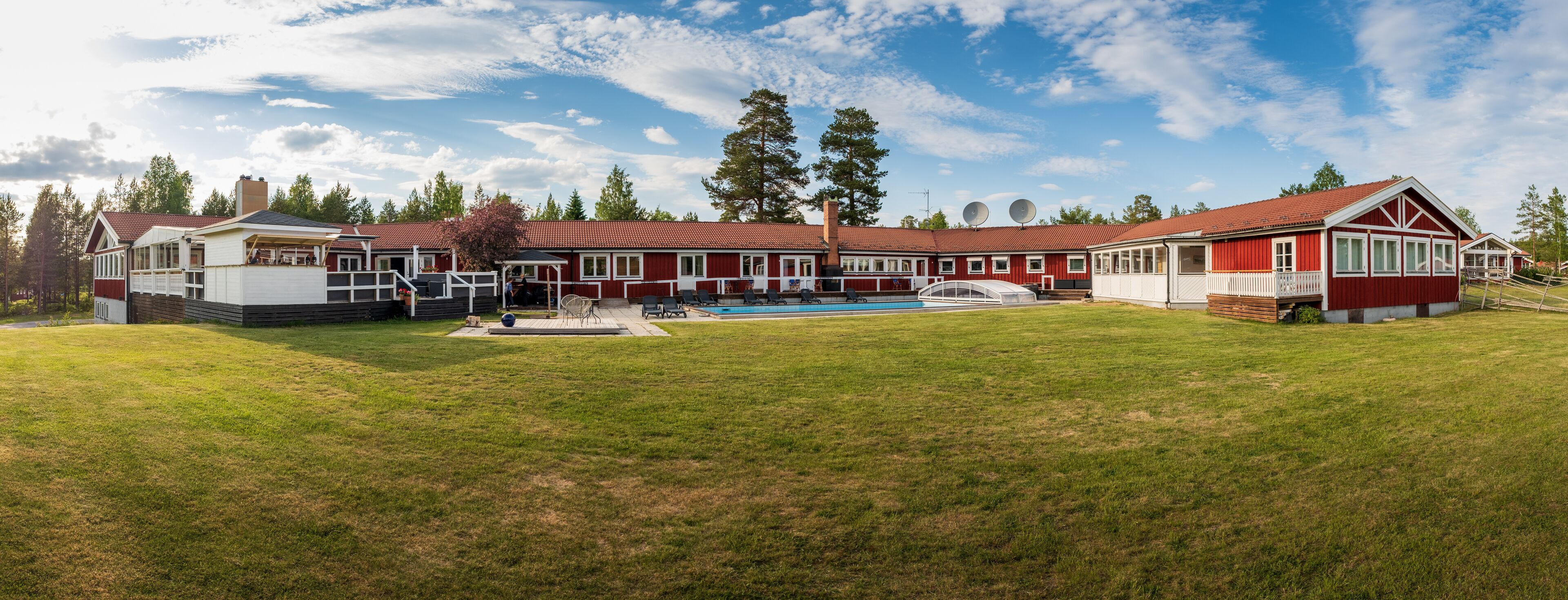 En stor byggnad i rött och vitt med en swimmingpool, omgiven av en gräsplätt och träd.