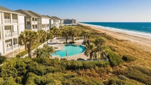 A resort with a pool surrounded by palm trees, overlooking a beach and ocean. - Oceanfront, Ocean Club F101, Linens included, 3Br 2ba, pool (Salter Path)