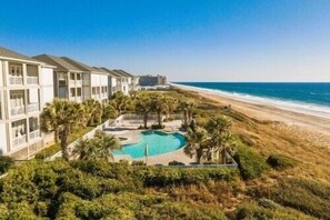 Een resort met een zwembad, omringd door palmbomen, met uitzicht op een strand en de oceaan.