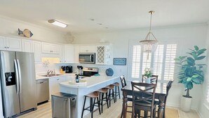 A modern kitchen with white cabinets, stainless steel appliances, and a central island with bar stools. - Oceanfront, Ocean Club F101, Linens included, 3Br 2ba, pool (Salter Path)