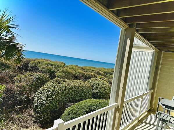 A wooden balcony with a view of the ocean and dense vegetation.
