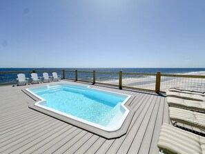 Una terraza de madera con un jacuzzi, sillas de descanso y vista al océano.