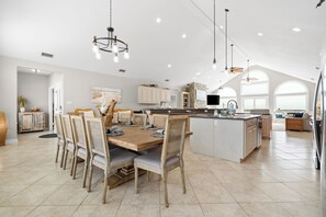 Una cocina amplia con una isla grande, electrodomésticos modernos y un comedor con sillas de madera y una mesa espaciosa.