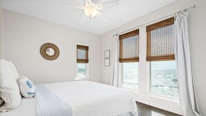 A bedroom with a bed, a ceiling fan, a window with a view of the sea, and a wall-mounted mirror.