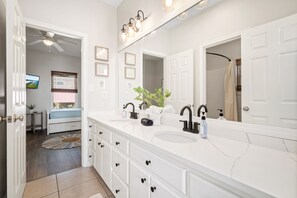 Un baño moderno con muebles blancos, dos lavamanos, un espejo grande y un ventilador de techo.