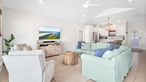 A modern living room with a large flat-screen TV, a white sofa, a light green sofa, and a wooden coffee table.