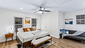 A bedroom with a bed, bedside tables, a bench, a ceiling fan, and artwork on the walls. - Grand Family Oasis – pool + game room (Houston)