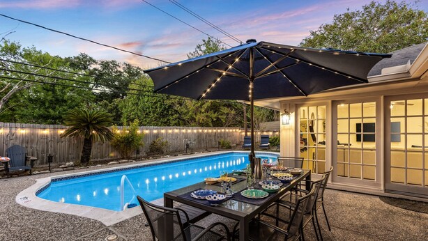 A backyard with a swimming pool, a covered patio table, and chairs. - Grand Family Oasis – pool + game room (Houston)