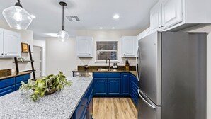 A kitchen with blue cabinets, a granite countertop, a stainless steel refrigerator, and pendant lighting. - Grand Family Oasis – pool + game room (Houston)