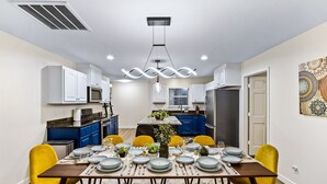 A modern kitchen with white cabinets, a central island, and a dining area with yellow chairs and a table set for six. - Grand Family Oasis – pool + game room (Houston)