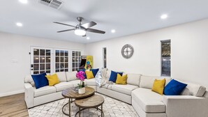 A living room with a sectional sofa, two round coffee tables, a ceiling fan, and a large window. - Grand Family Oasis – pool + game room (Houston)