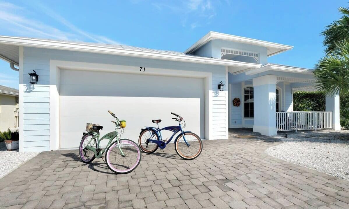 Une maison à deux étages avec un garage, deux vélos garés devant et une allée bien entretenue.