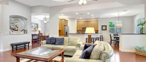 A spacious living room with a ceiling fan, a glass coffee table, and a seating area with a sofa and armchairs.