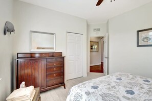 Ein Schlafzimmer mit einem großen Bett, einer Holzkommode, einem Spiegel und einer Tür zu einem weiteren Raum.