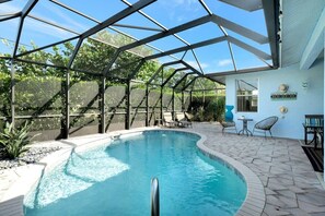 Ein Schwimmbad mit Glasveranda, umgeben von einer Terrasse mit Gartenmöbeln.