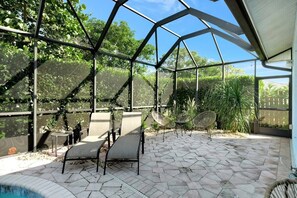 Une serre dotée d’un sol en pierre hexagonale, de chaises à structure métallique et d’un toit en verre.
