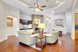 A spacious living room with a fireplace, two sofas, a coffee table, and a ceiling fan.