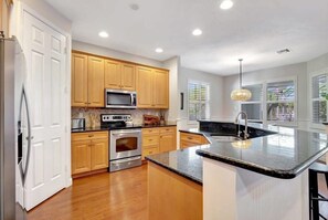 A modern kitchen with wooden cabinets, stainless steel appliances, and a large island with a black countertop.