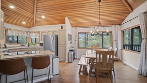 Eine moderne Küche mit Holzbalkendecke, einer zentralen Kochinsel mit Barhocker und einem Essbereich mit Holztischen und Stühlen.
