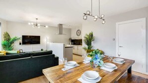 A modern living room with a wooden dining table set for four, a dark green sofa, and a kitchen in the background. - Host & Stay | Ropewalks Quarters III (Liverpool)