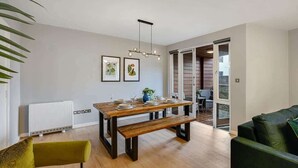 A modern dining area with a wooden table, bench, and green chairs. There are framed pictures on the wall and a plant on the table. - Host & Stay | Ropewalks Quarters III (Liverpool)