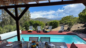 A poolside dining area with a table set for two, overlooking a pool and lounge chairs. - Villa Avec Piscine, en Pleine Nature et a 5 Minutes de Saint Florent ! (Santo-Pietro-di-Tenda)