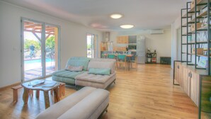 A spacious living area with a sofa, ottoman, and a dining table. - Villa Avec Piscine, en Pleine Nature et a 5 Minutes de Saint Florent ! (Santo-Pietro-di-Tenda)