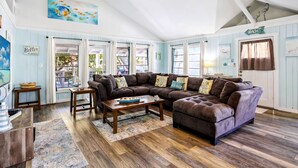 A cozy living room with a sectional sofa, wooden flooring, and a view of the outdoors.