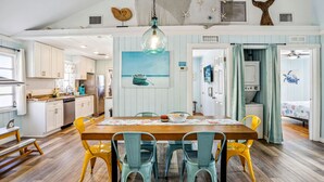 A spacious kitchen with a wooden table and yellow chairs, a dining area with a view of the living room, and a ceiling fan.