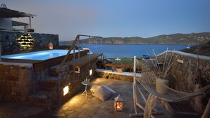 En stenterrasse med jacuzzi, hængekøje og et lille bord med stearinlys.