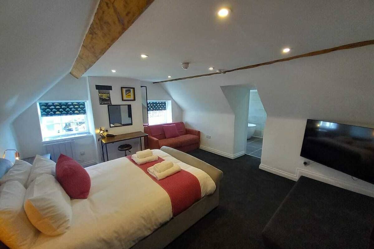 A hotel room with a large bed, a sofa, a TV, and a small kitchenette.