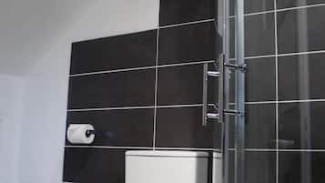 Et moderne badeværelse med toilet, skraldespand og brusekabine i glas.