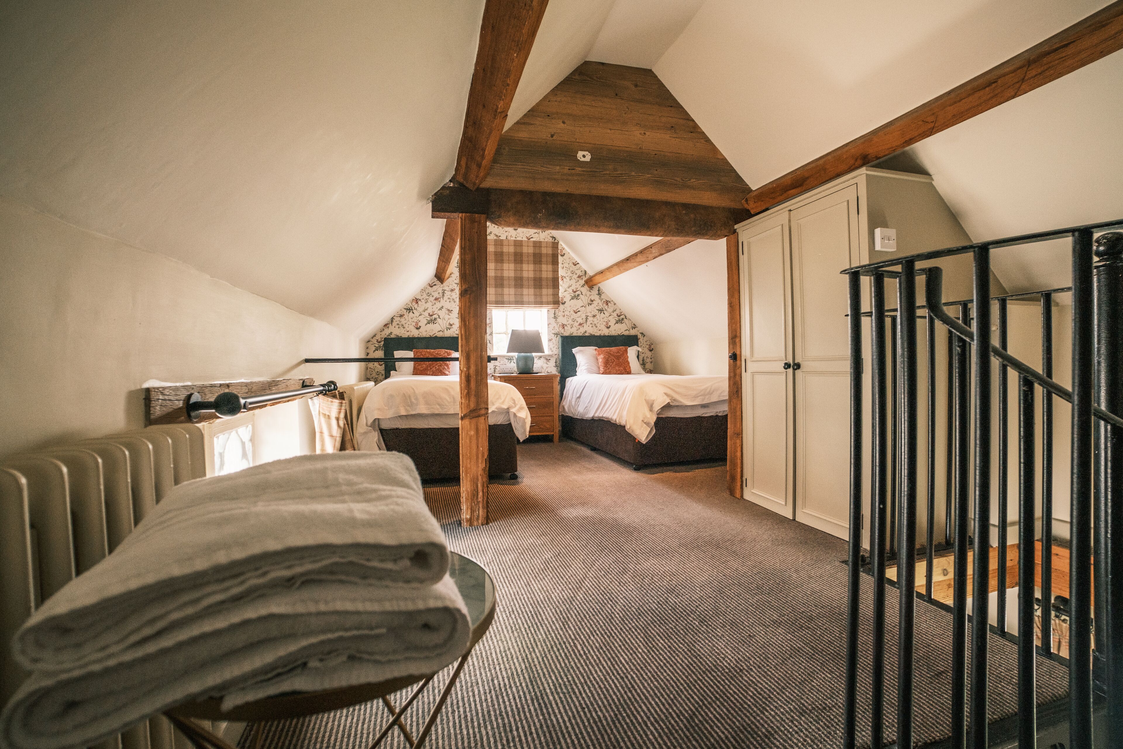 A cozy attic bedroom with two beds, a radiator, and a wooden ceiling.