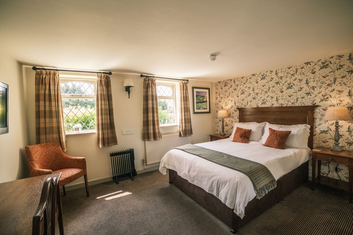 A bedroom with a large bed, a chair, a radiator, and a window with curtains.