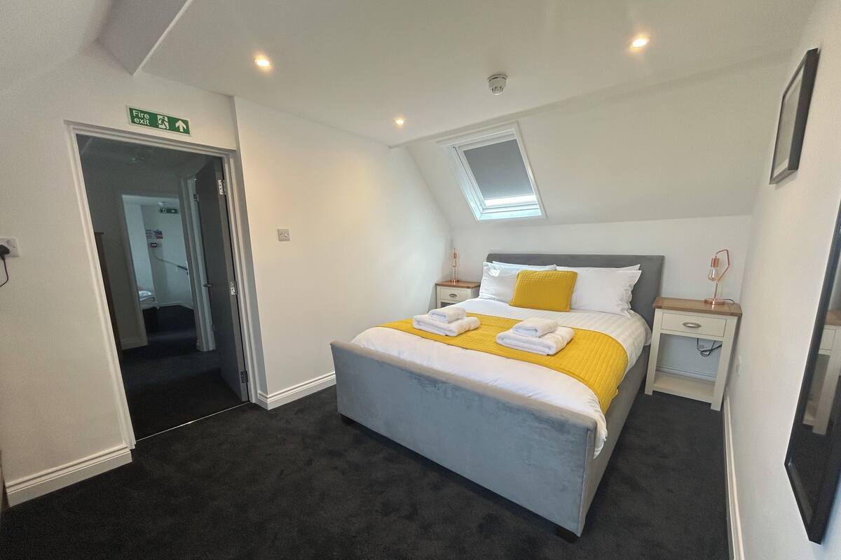A hotel room with a bed, a bedside table, a nightstand, a window, and a door.