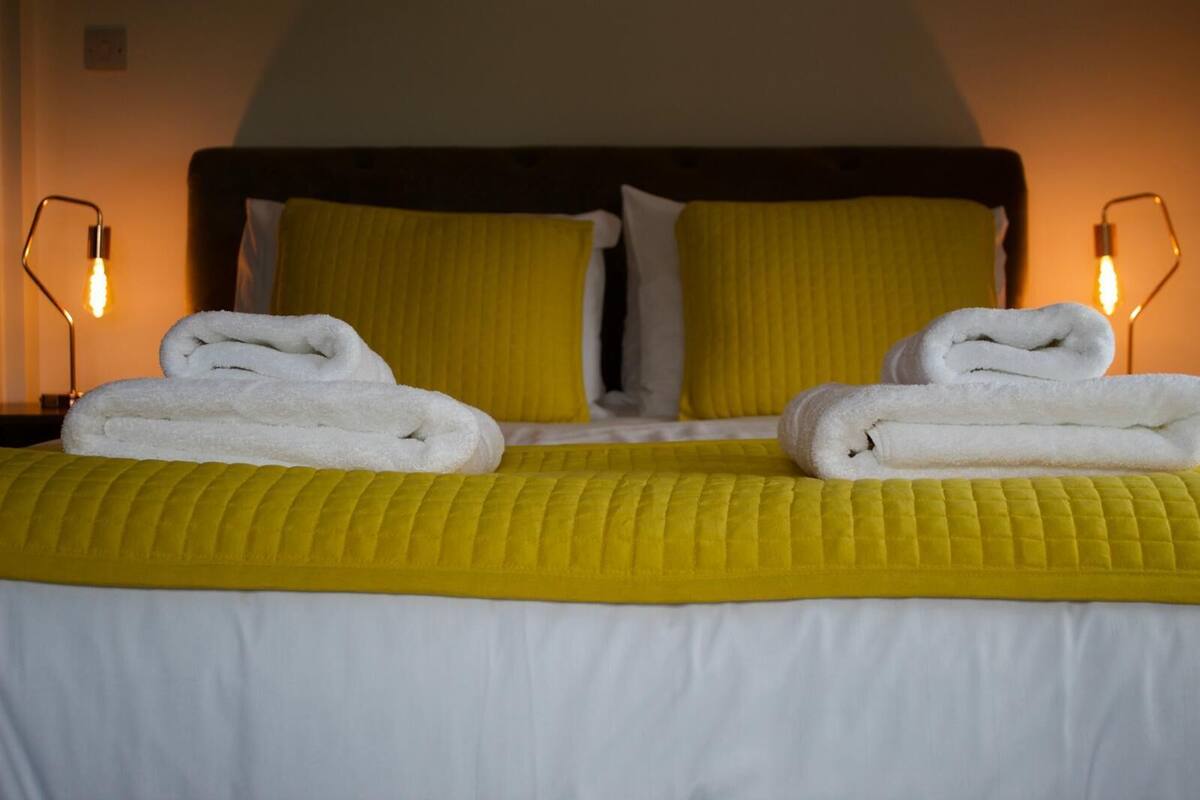 A hotel room with a bed, two pillows, two folded towels, and two bedside lamps.