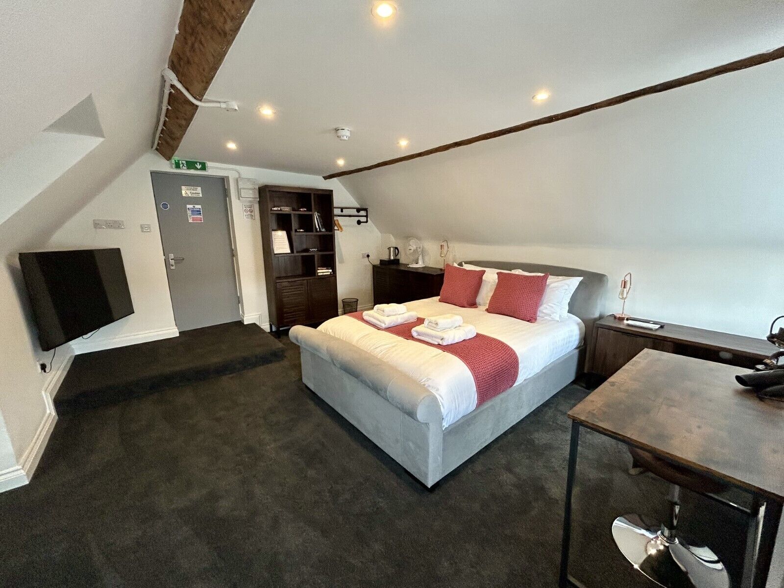 Una habitación de hotel con cama, escritorio, televisor, estantería y perchero.