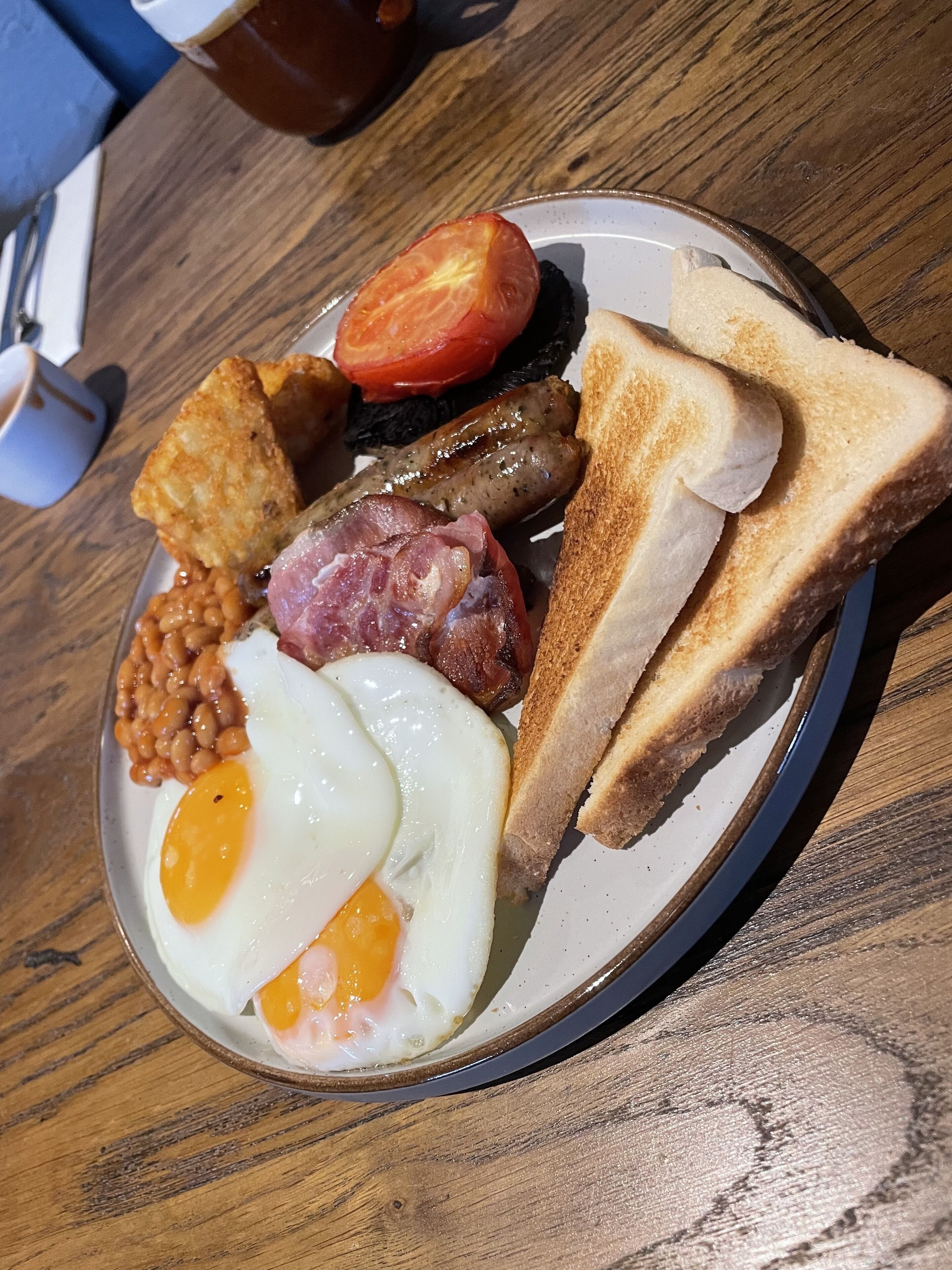 A plate of breakfast food including eggs, sausages, beans, toast, and a tomato.