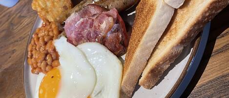 A plate of breakfast food including eggs, sausages, beans, toast, and a tomato.