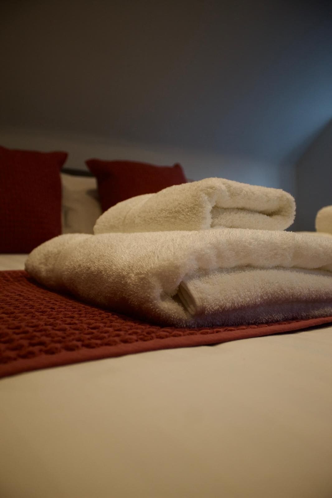 A neatly folded white towel on a bed with a red blanket.