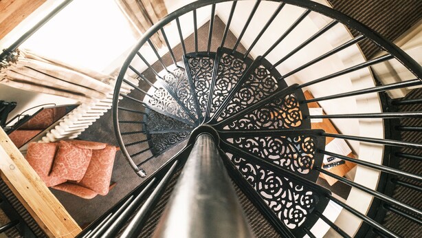A spiral staircase with ornate metal railings and a wooden handrail. - The Stag (Alcester)