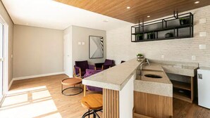 A modern kitchen with a wooden ceiling, white brick wall, and a built-in island with a sink. - Studio de Luxo de Alta Qualidade (Bela Vista São Paulo)