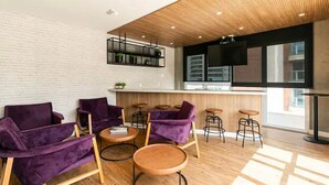 A modern lounge area with purple sofas, wooden tables, and a kitchen area with a bar. - Studio de Luxo de Alta Qualidade (Bela Vista São Paulo)