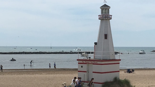 Eine Strandansicht mit einem Leuchtturm, sandigem Ufer und Menschen.